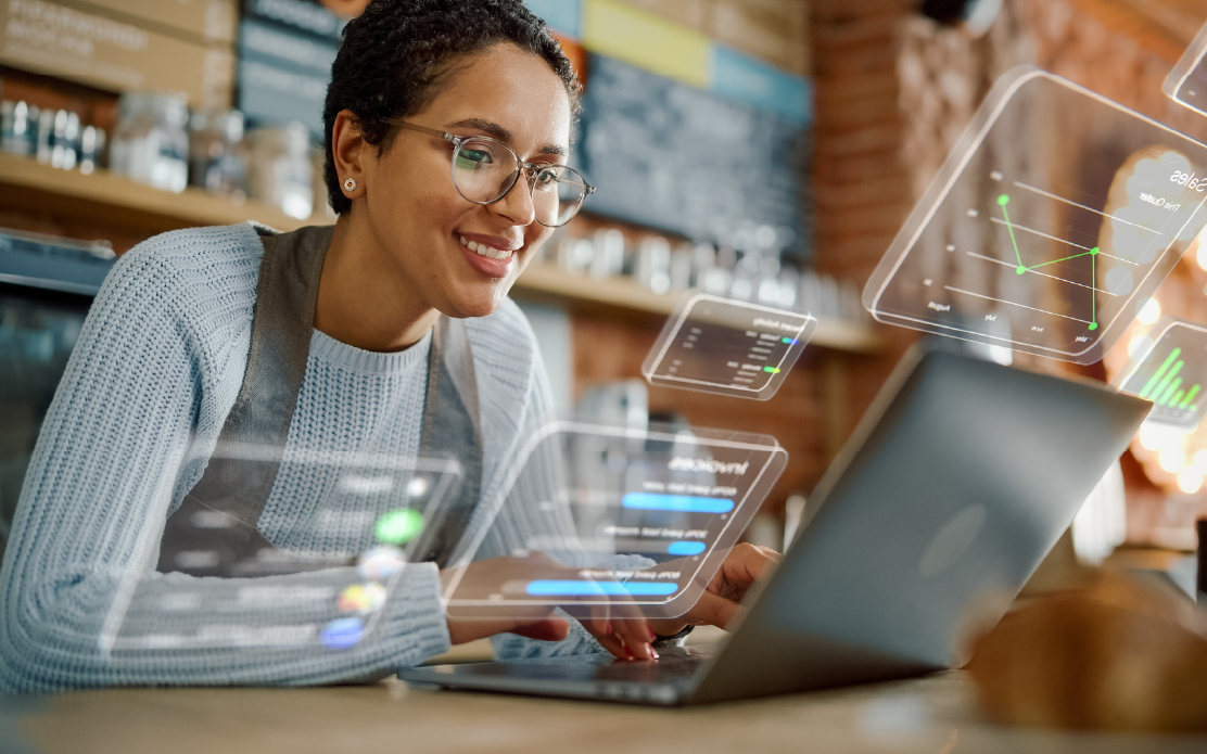 Person smiling while using a laptop at a table with floating digital interface graphics.