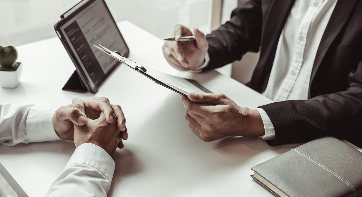 Business meeting with hands around a laptop and tablet on a white desk, discussing documents.