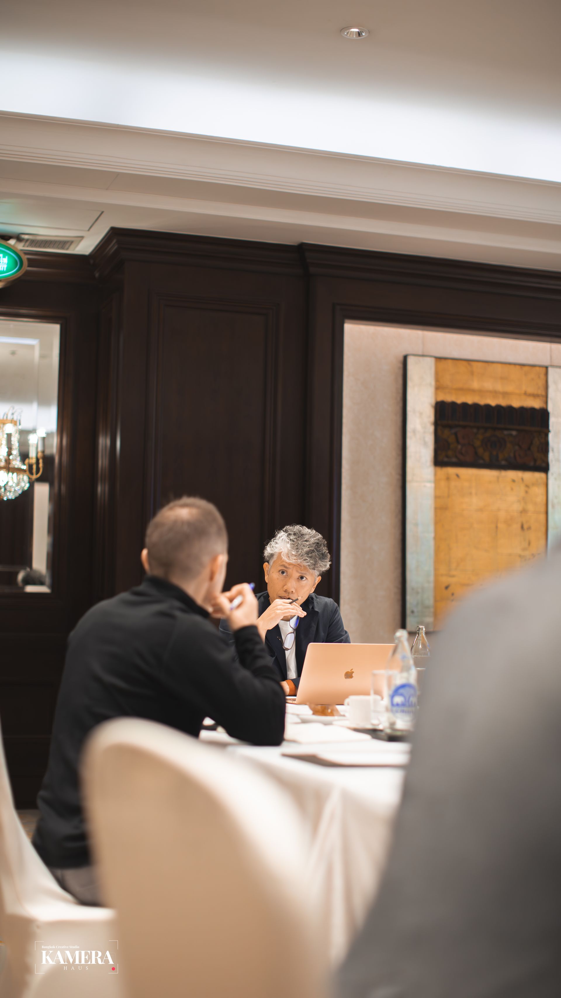 People seated at a conference table in a formal meeting room, with laptops and papers in front of them.