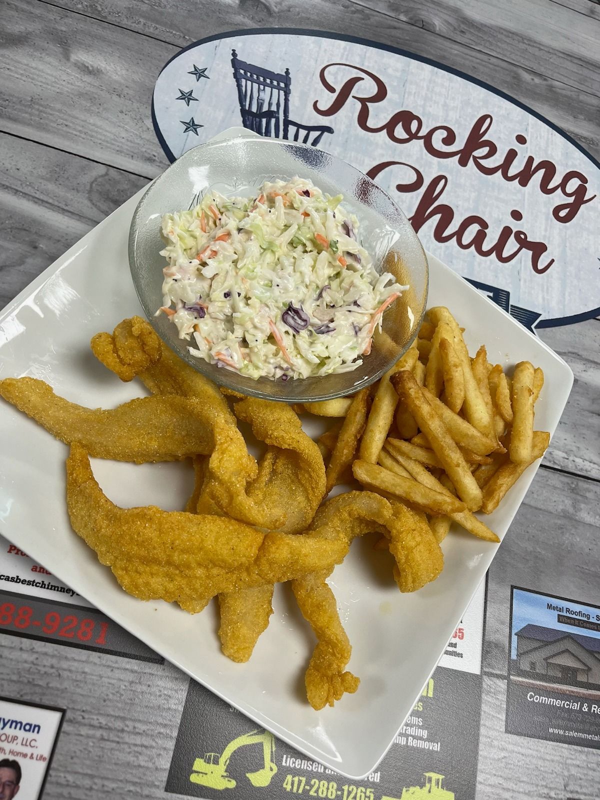 Basket of fried fish, French fries, and coleslaw on newspaper-lined table at Rocking Chair restaurant.