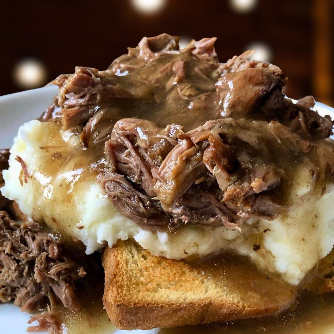 Toasted bread topped with mashed potatoes and shredded beef gravy on a white plate