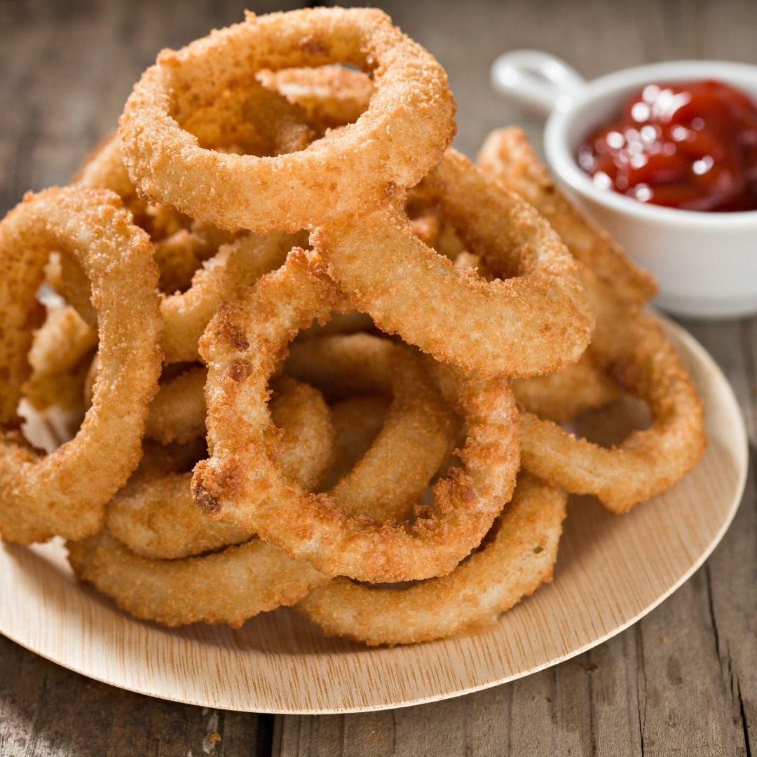 Plate of crispy fried onion rings with a side of ketchup on a wooden table