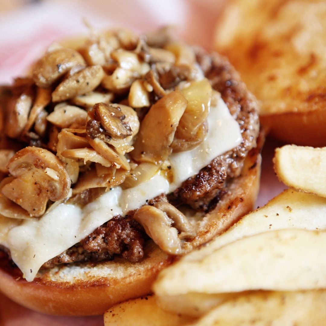 Mushroom and cheese burger with potato chips on a plate.