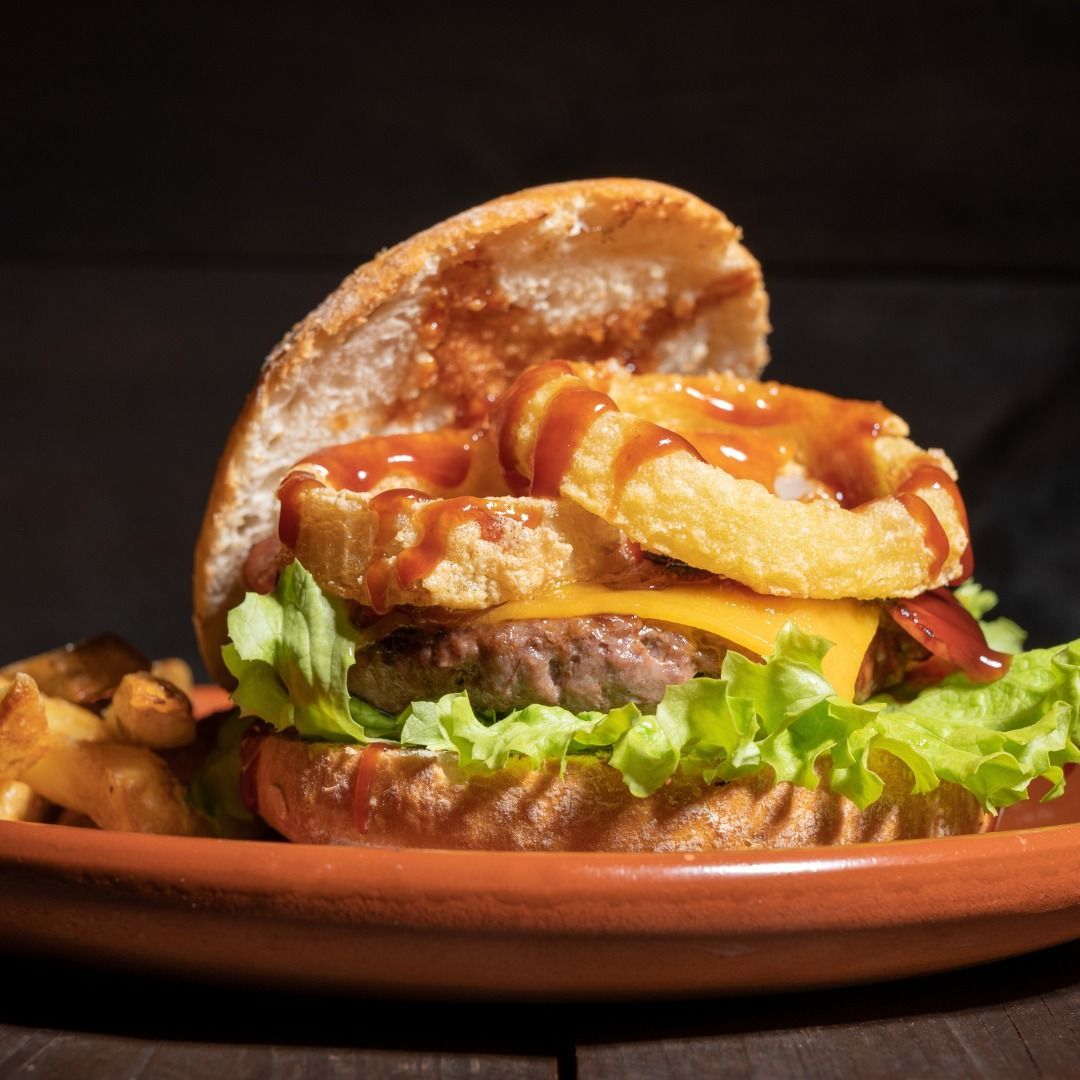 Burger with lettuce, tomato, cheese, fries, and ketchup on a plate against a dark background