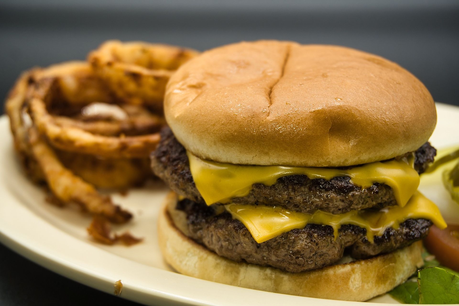 Cheeseburger on a plate with onion rings in the background