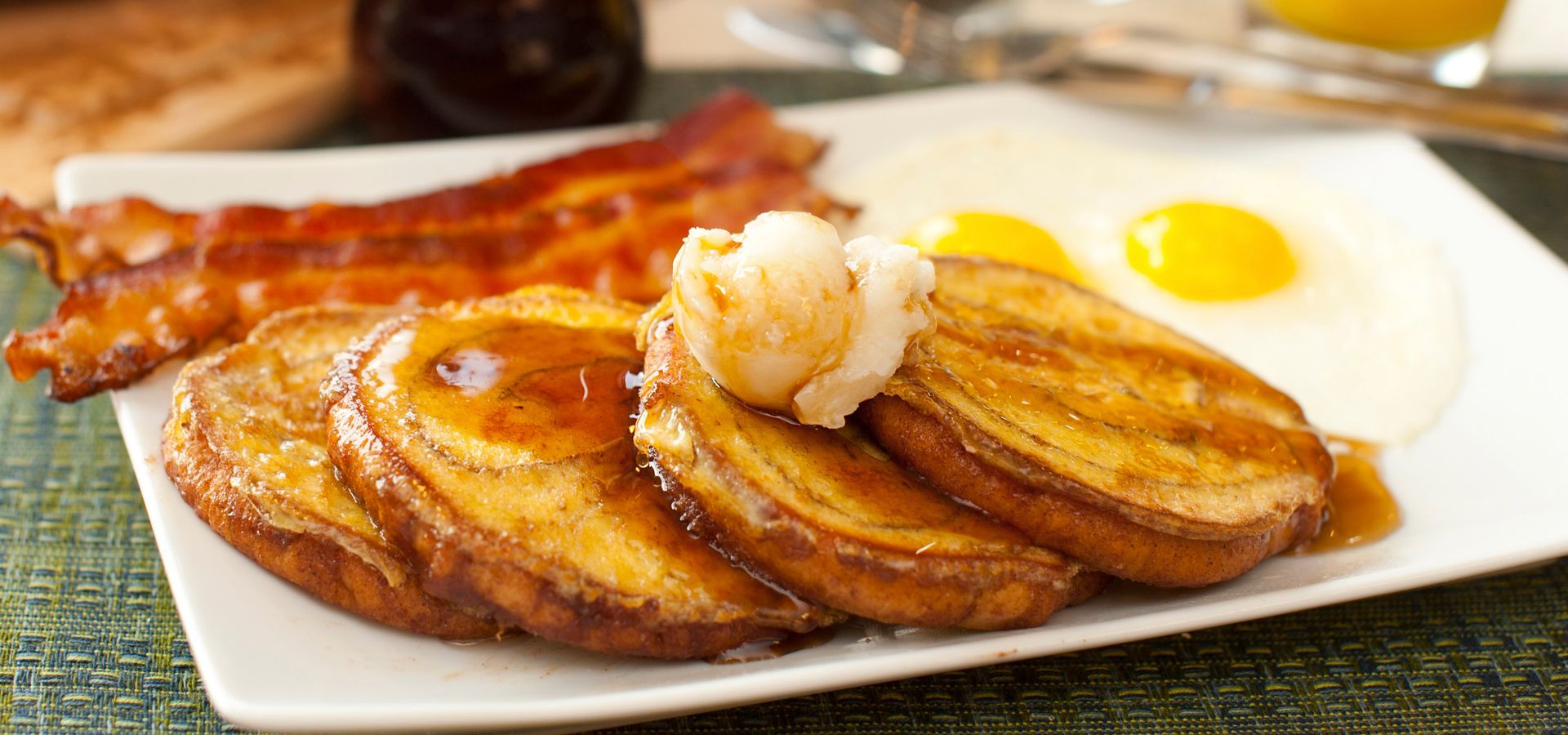 Plate of pancakes with bacon, eggs, and a dollop of butter on a table