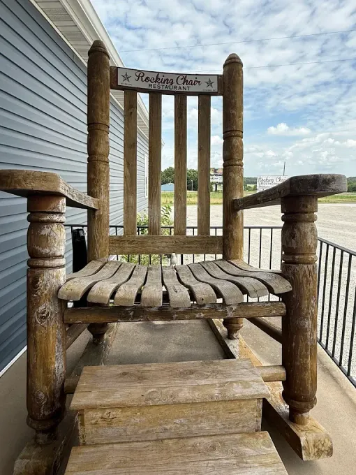 Weathered wooden rocking chair on a porch beside gray siding under a cloudy sky