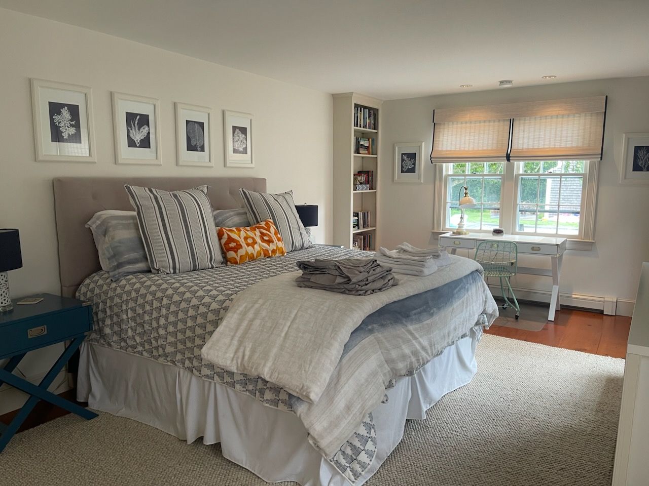 Bright bedroom with a gray bed, white rug, desk by the window, and framed wall art