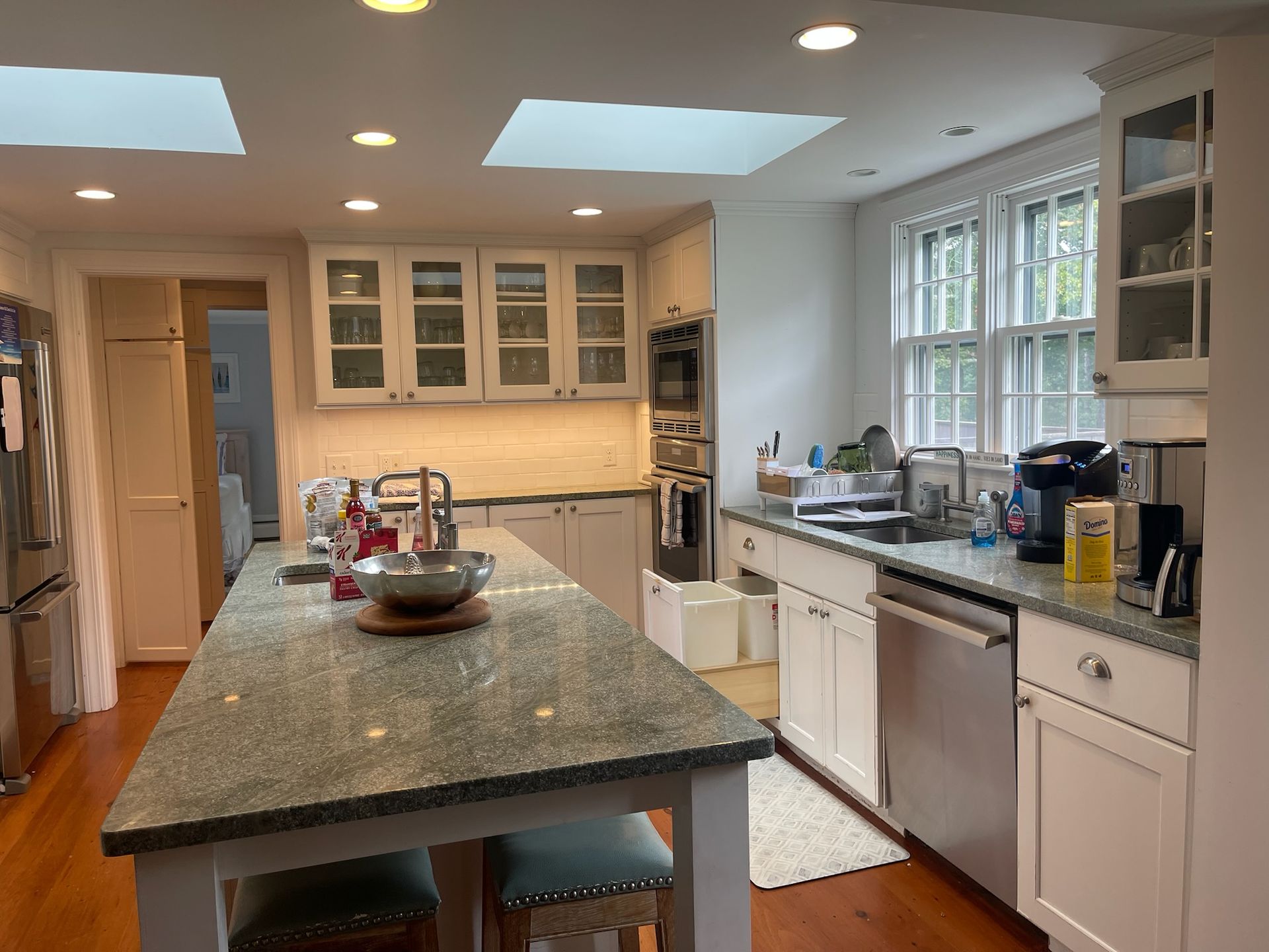 Bright kitchen with granite island, white cabinets, stainless appliances, and large windows on the right.