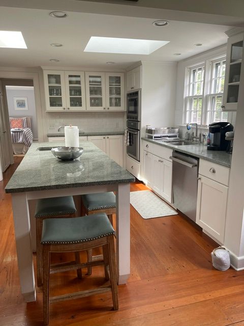 Bright kitchen with island, white cabinets, hardwood floors, and daylight from large windows.