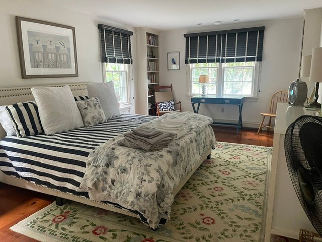 Bedroom with striped bedspread, floral rug, window seats, and a desk by two windows