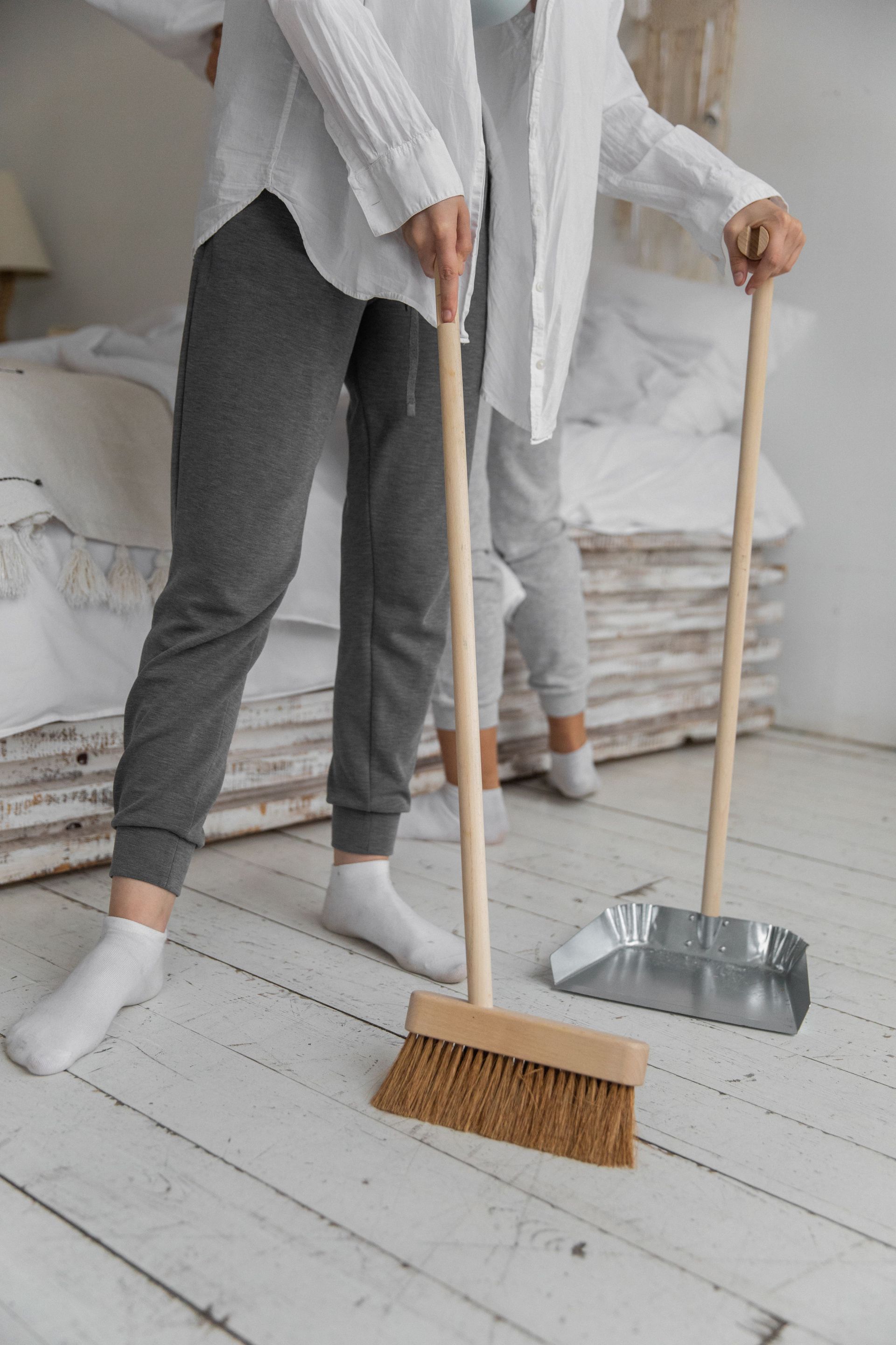 Two people sweeping a white wooden floor in a bright room