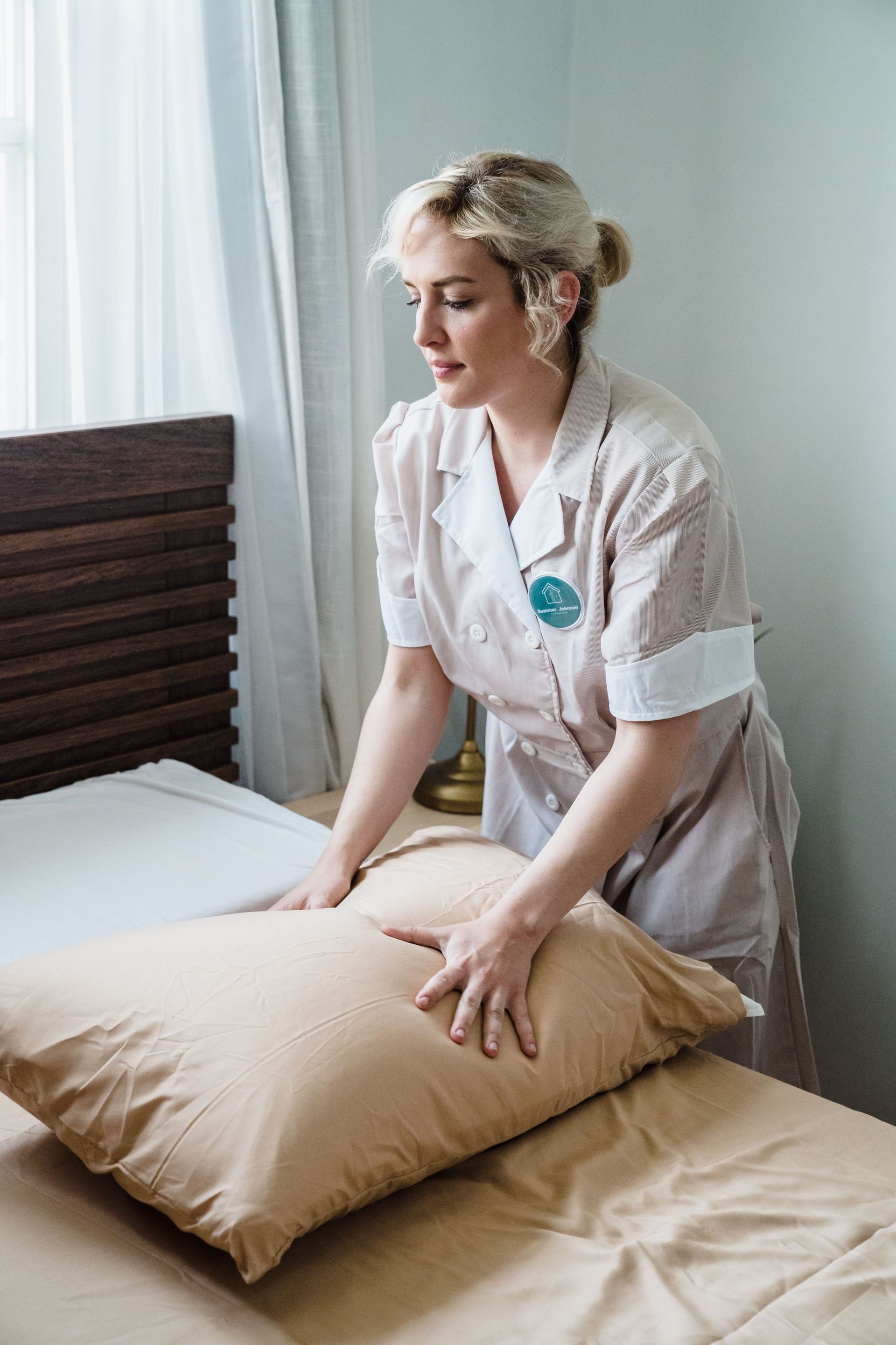 Caregiver adjusting a pillow on a bed in a bright bedroom