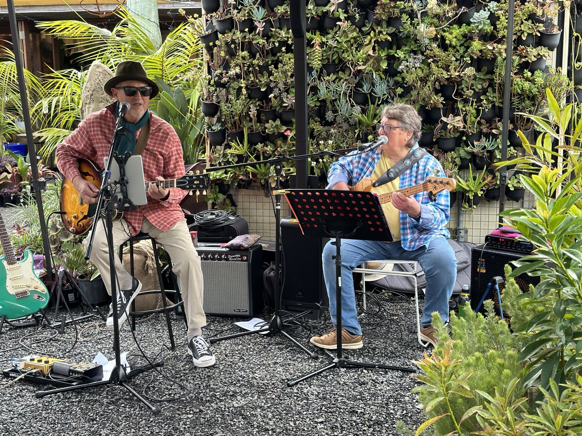 Two Men Are Playing Guitars And Singing Into Microphones In A Garden — Burnetts On Barney in Kiama, NSW