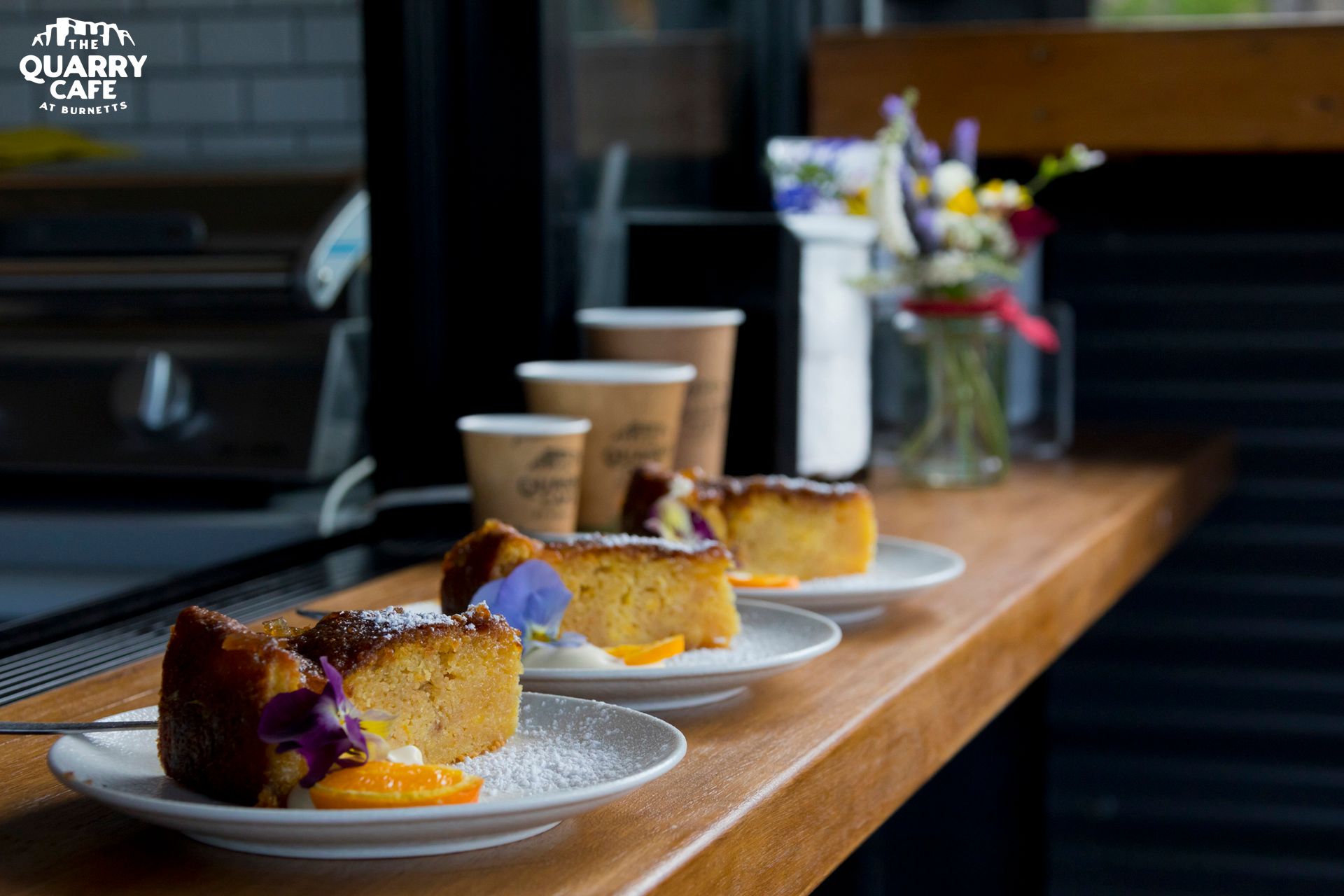 A Row Of Plates With Slices Of Cake On Them On A Wooden Counter — Burnetts On Barney in Gerringong, NSW