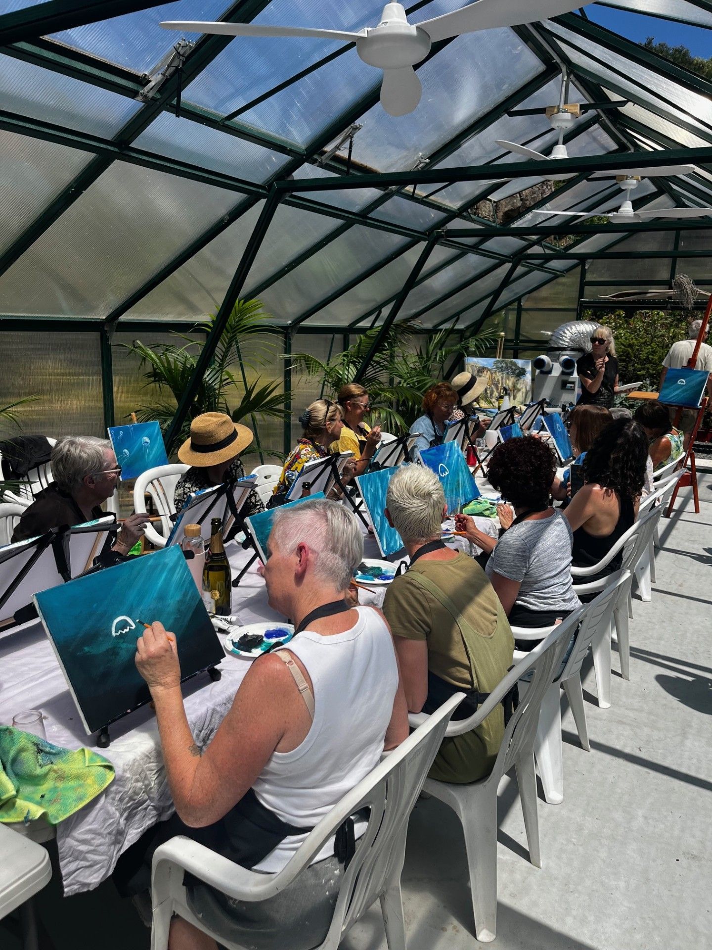 A Group Of People Are Sitting At Tables In A Greenhouse Painting — Burnetts On Barney in Kiama, NSW