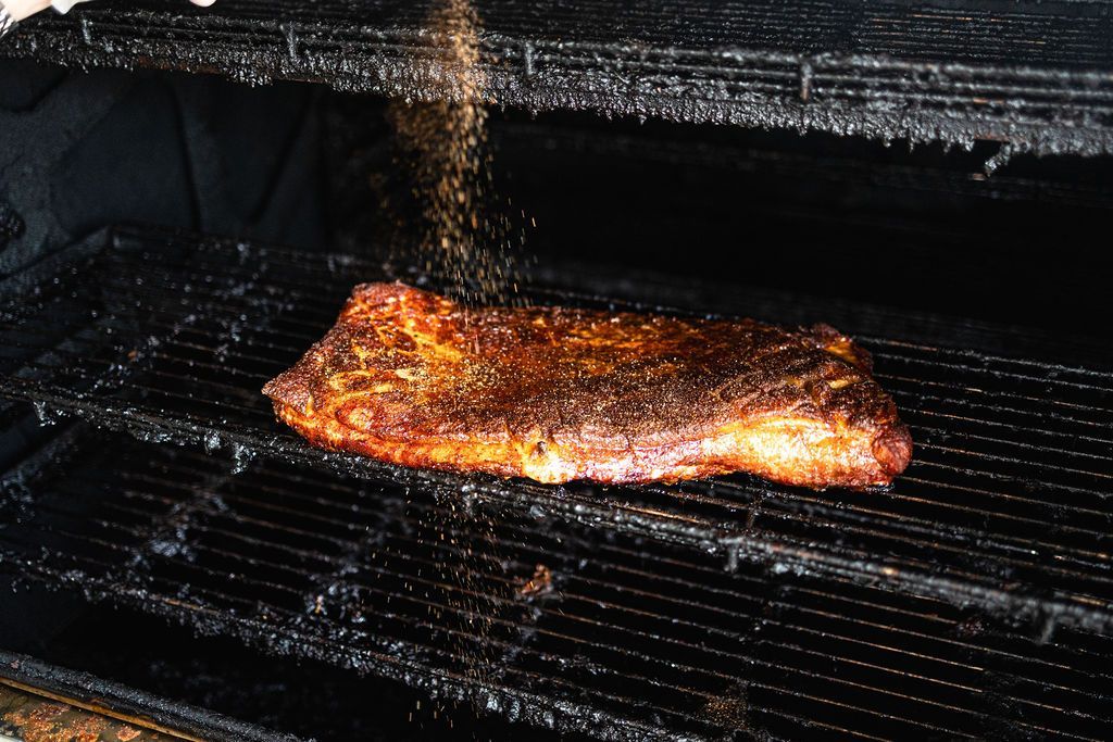 A slab of meat sizzling on a grill with flames and smoke rising