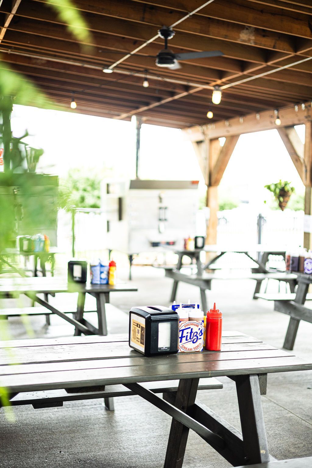 Open-air picnic tables under a wooden pavilion with condiment bottles on a table