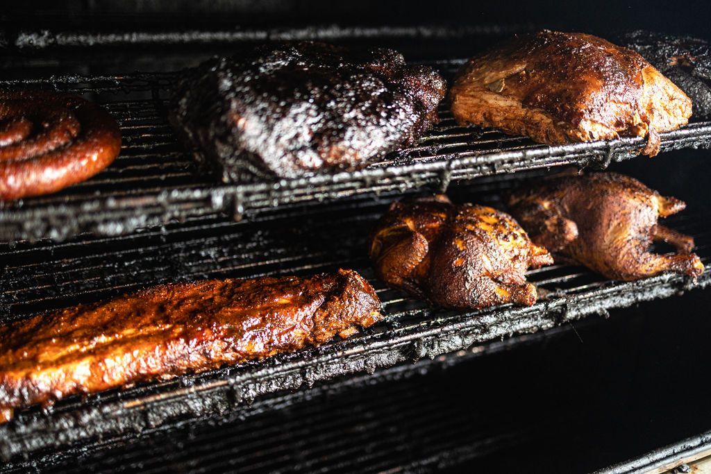 Meat smoking on racks in a dark barbecue smoker, with charred, glossy surfaces