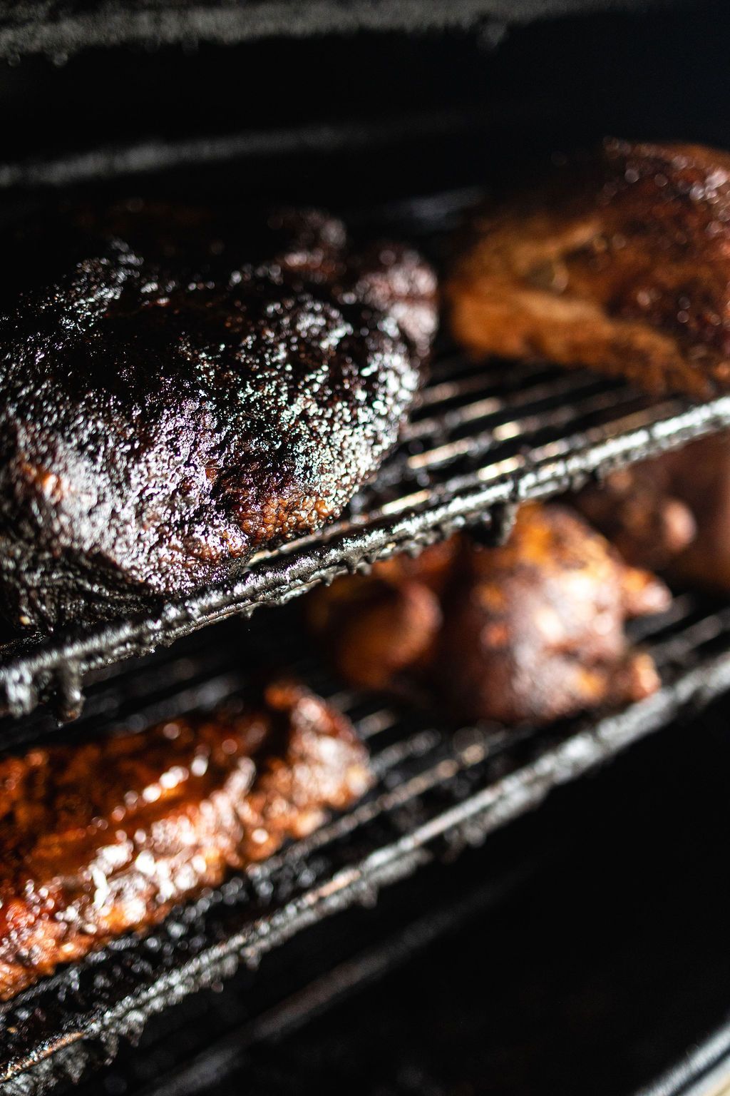 Smoky barbecue meats on metal smoker racks, with glistening charred surfaces