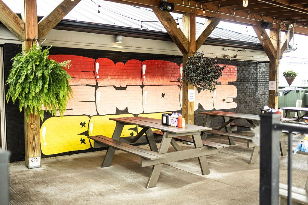 Covered picnic area with wooden tables, hanging fern, and colorful painted wall