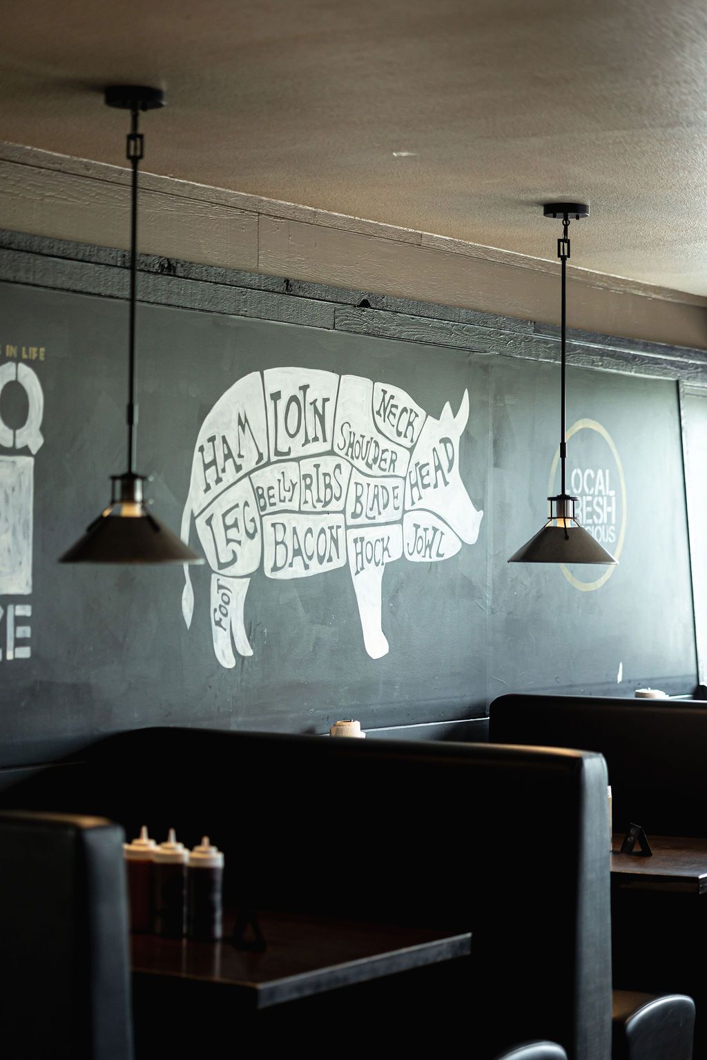 Dim restaurant booth seating with hanging lamps and a white pig mural on a gray wall.