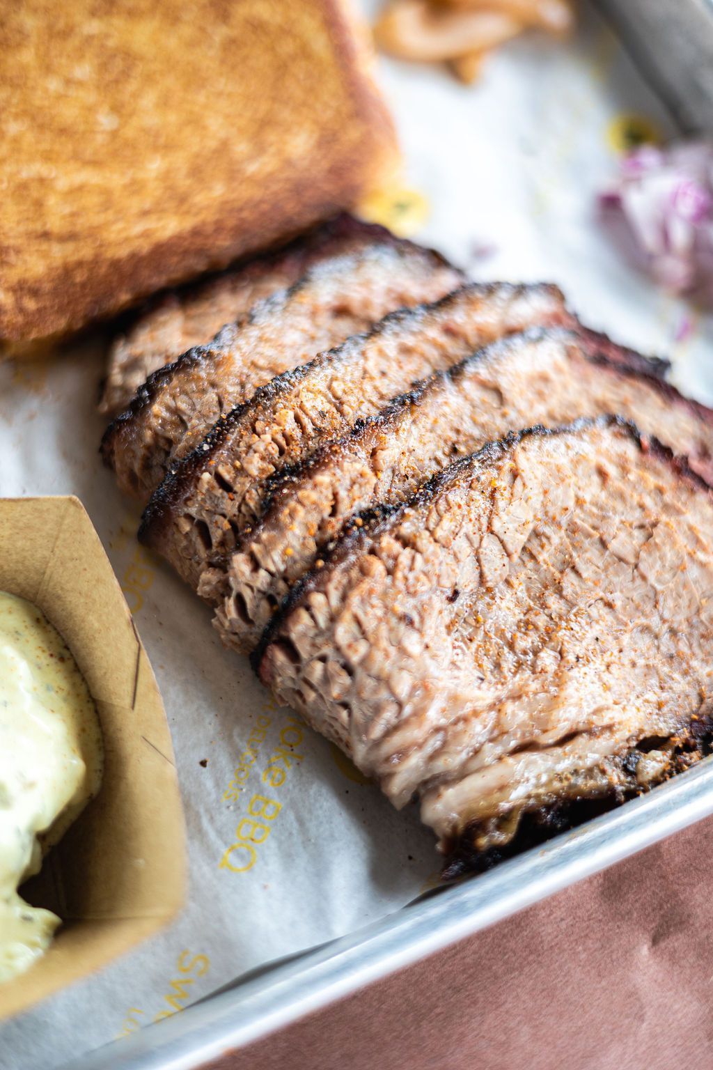 Sliced roasted meat in a metal tray with a browned loaf and a side of sauce