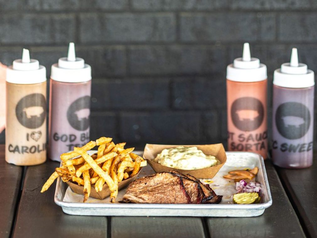 BBQ tray with fries, coleslaw, corn, ribs, and four labeled sauce bottles on a table