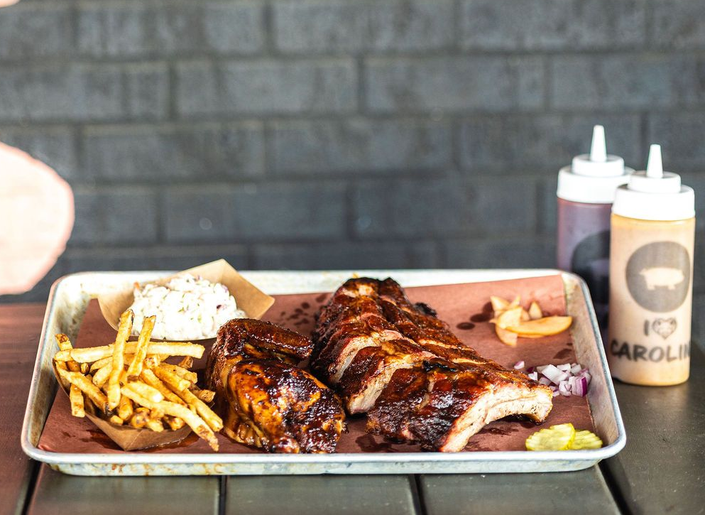 Tray of barbecue ribs with fries, coleslaw, and sauces on a table