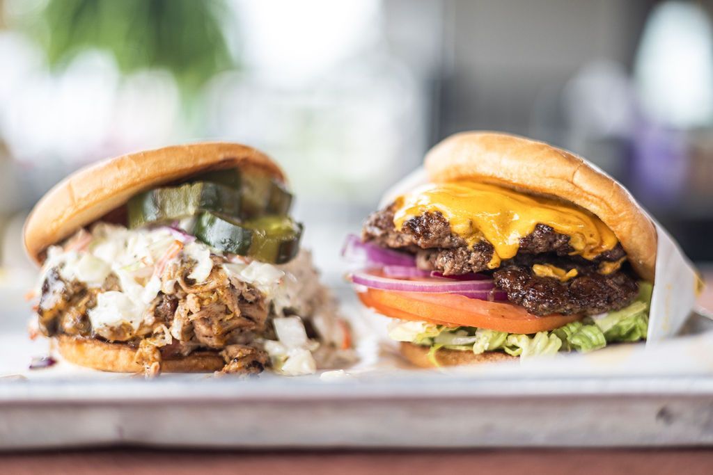 Two gourmet burgers on a tray, one with melted cheese and bacon, against a blurred background