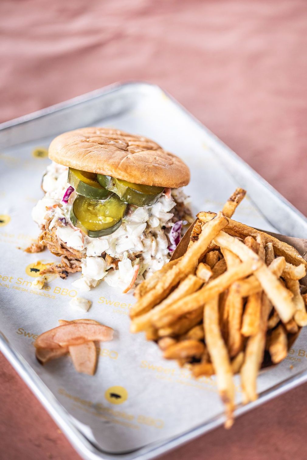 Burger with fries on a metal tray, with a bit of sauce spilled on the side