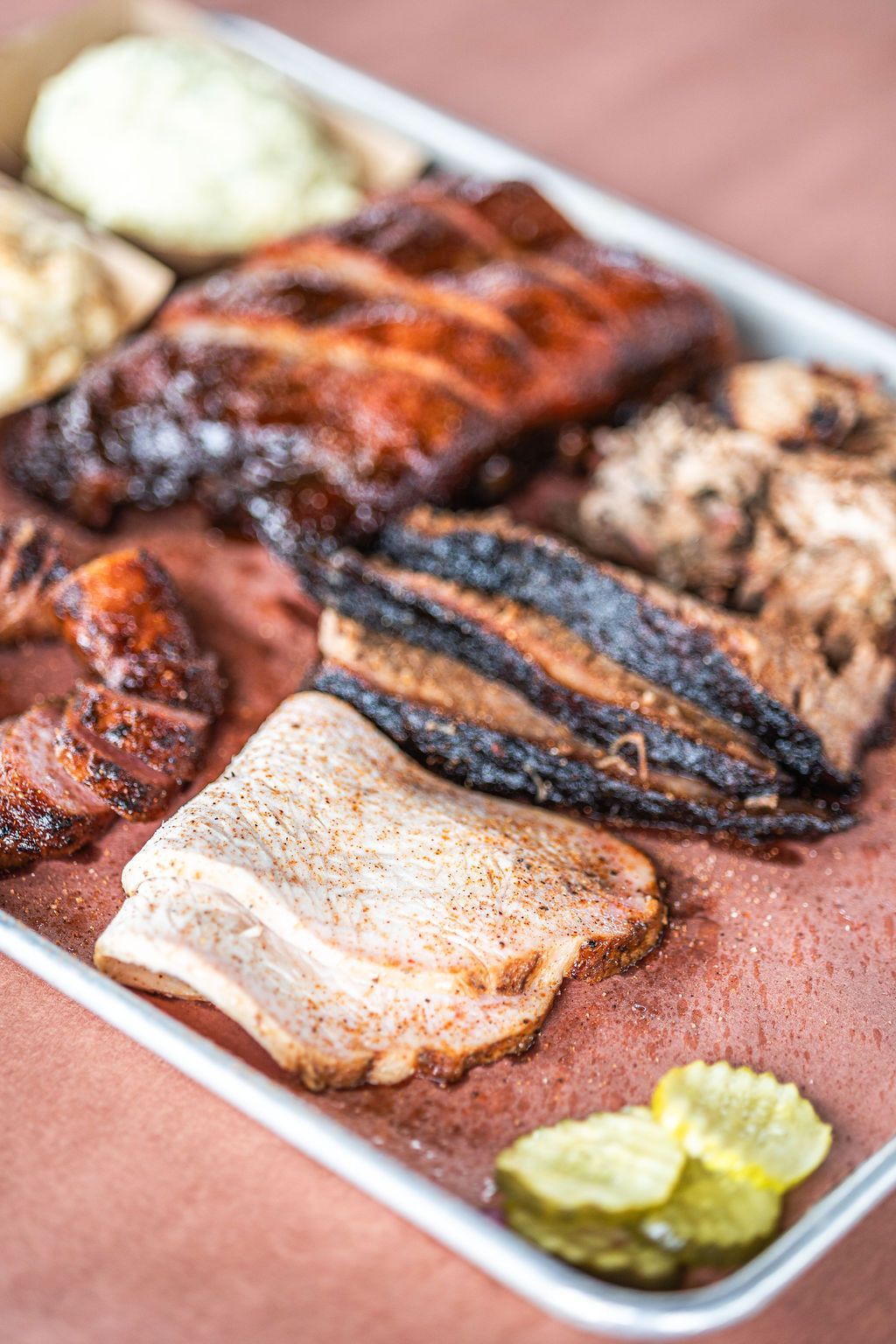 Assorted grilled meats on a platter with pickles and lemon wedges