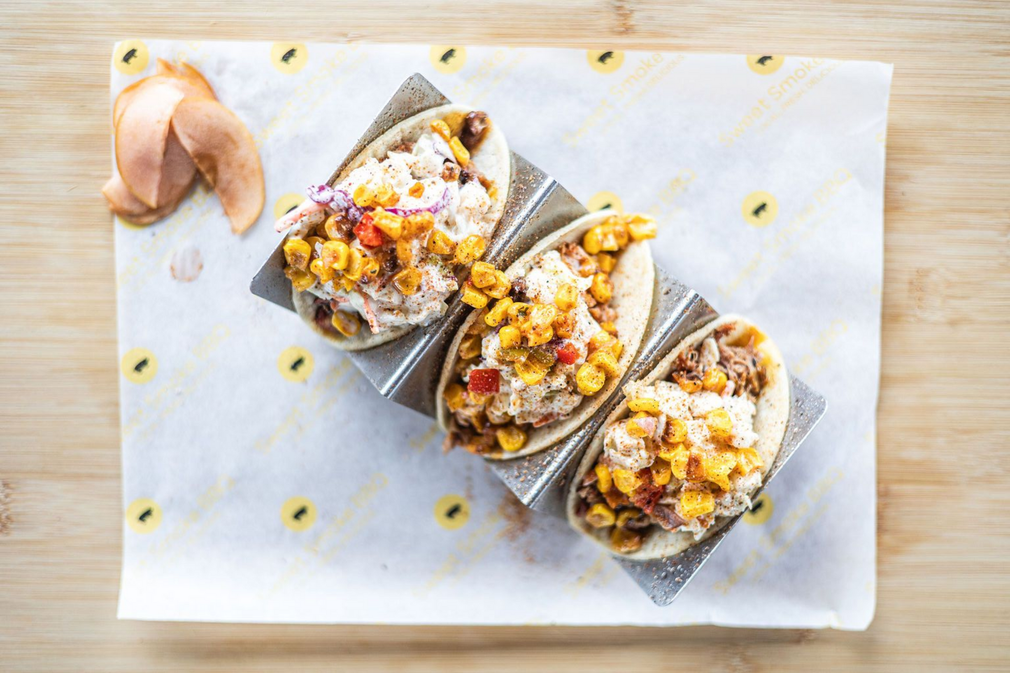 Three tacos on a white board with a creamy sauce and scattered yellow garnish