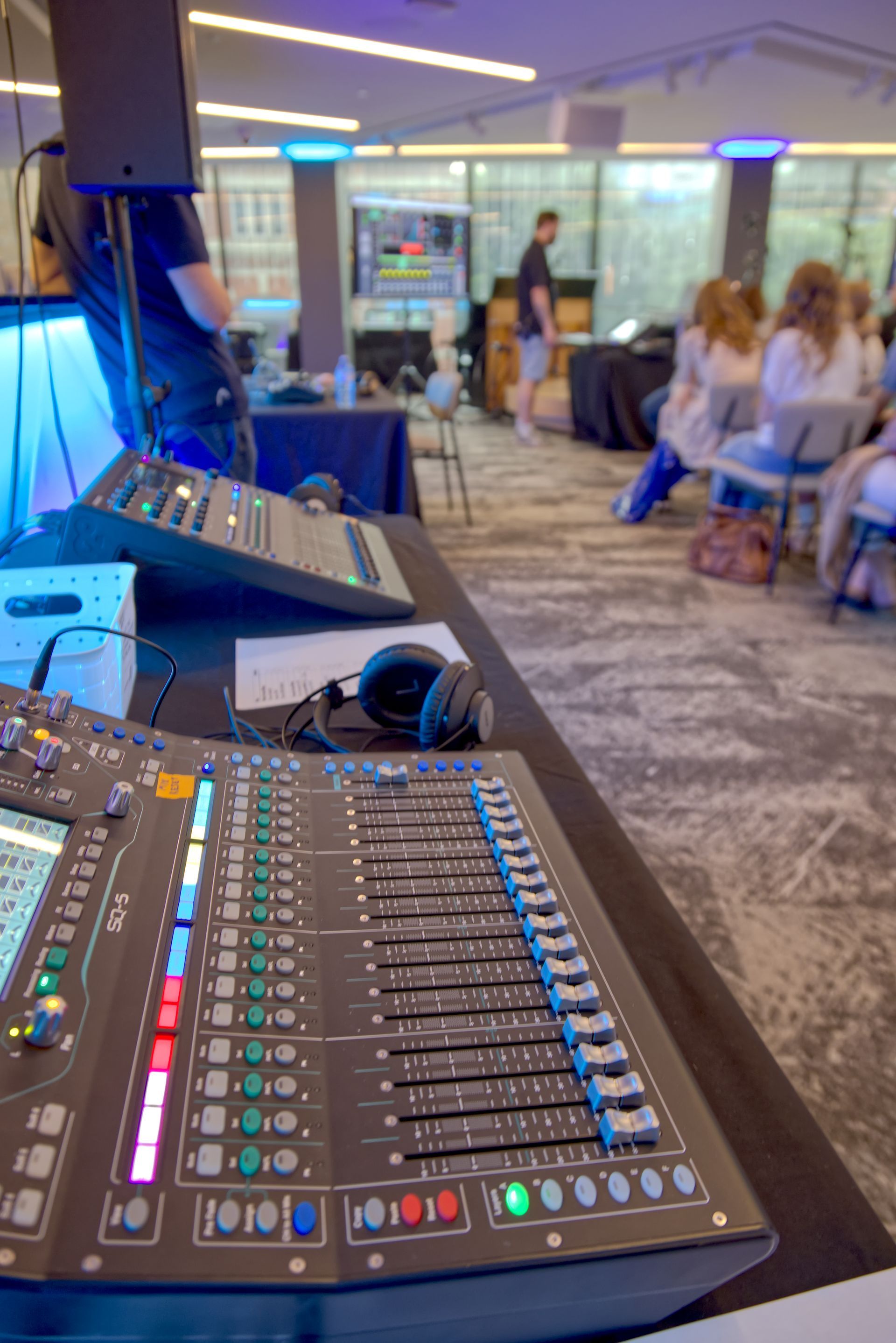 Sound mixing consoles on a table, with people in the background, likely at an event or performance.
