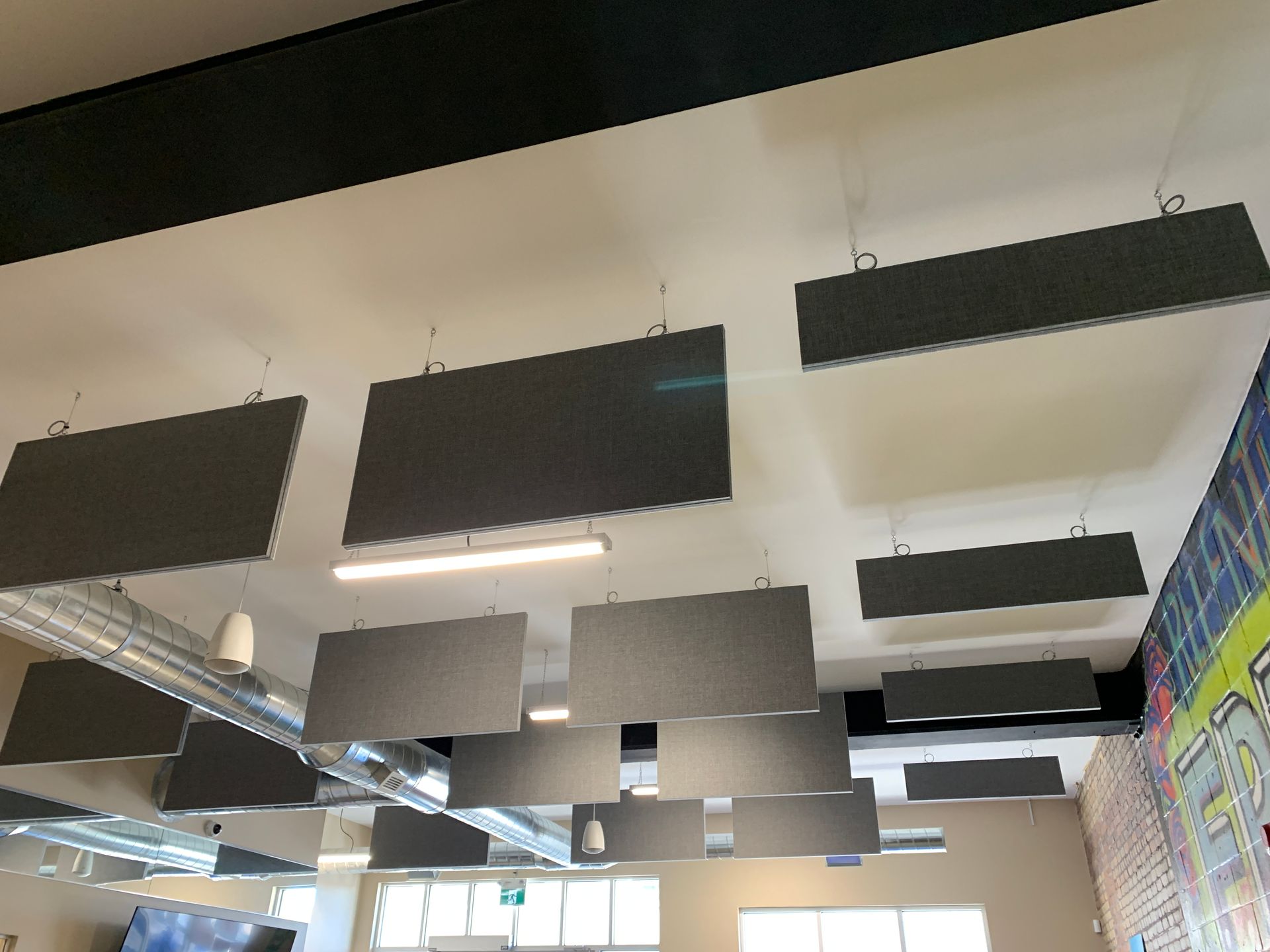 Gray rectangular acoustic panels suspended from a white ceiling, installed in an office space.