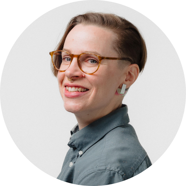 Person with short hair and glasses smiling, wearing a blue shirt.