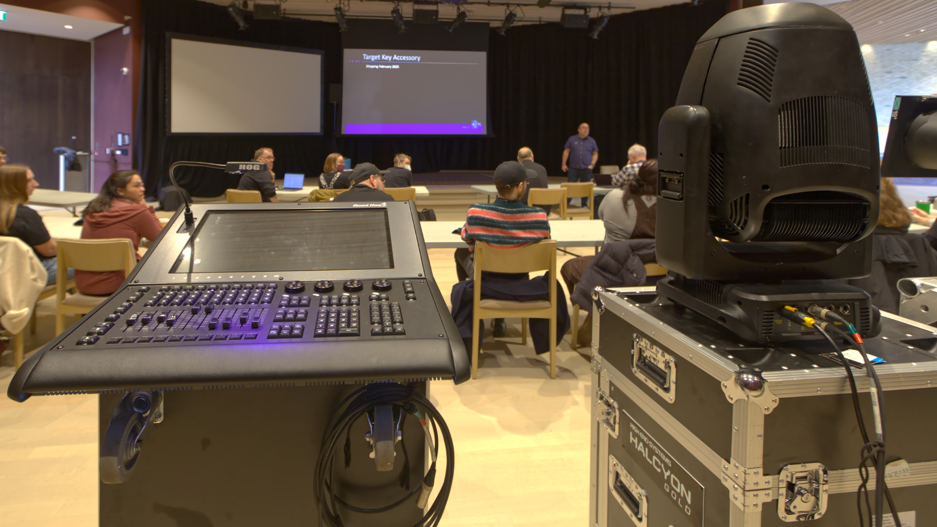 Control panel, spotlight, and people at a presentation in an auditorium.