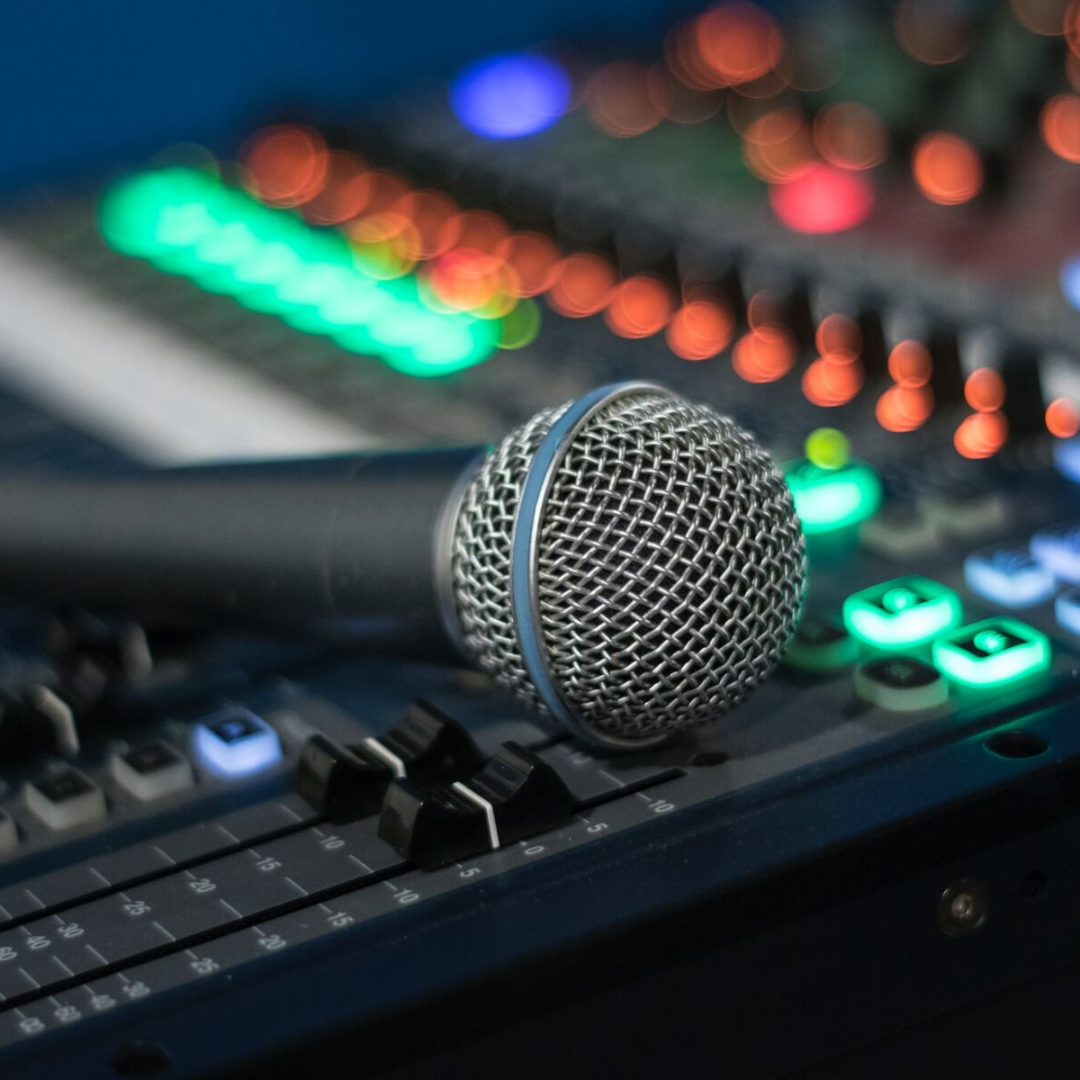 Microphone resting on audio mixing board; blurred lights in background.