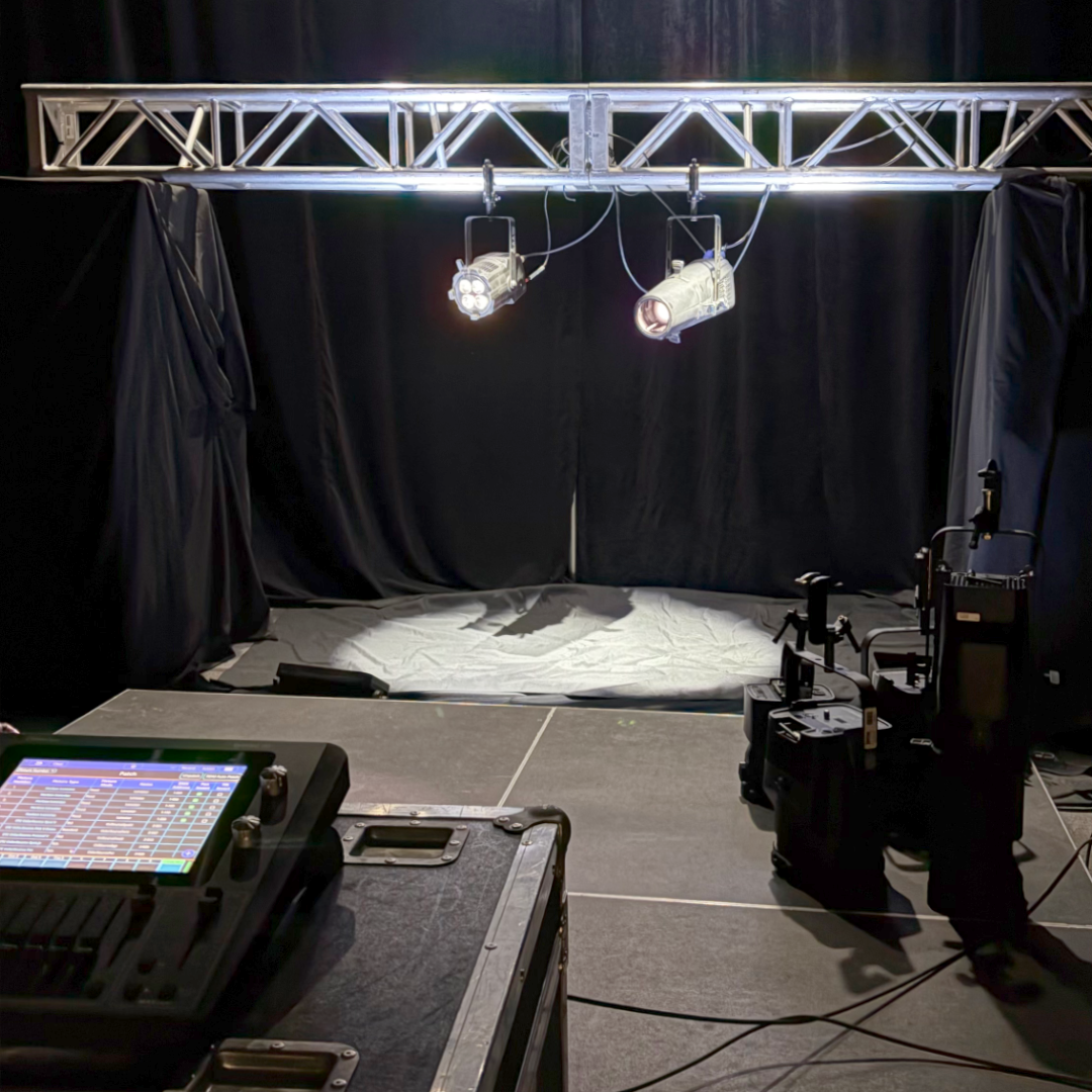 Stage with lighting equipment, including spotlights on a truss and a control board.