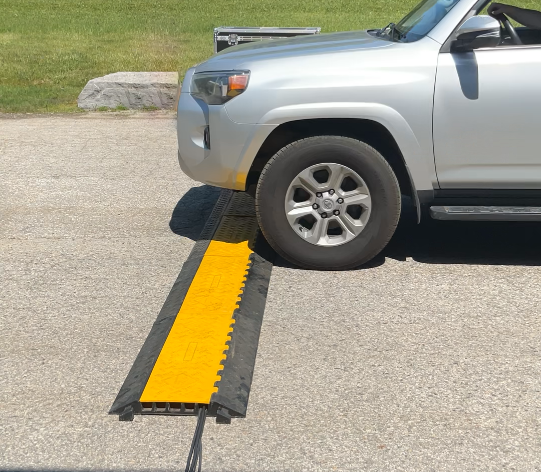 Silver SUV drive over a cable mat in an outdoor parking lot, with grass and trees in the background.