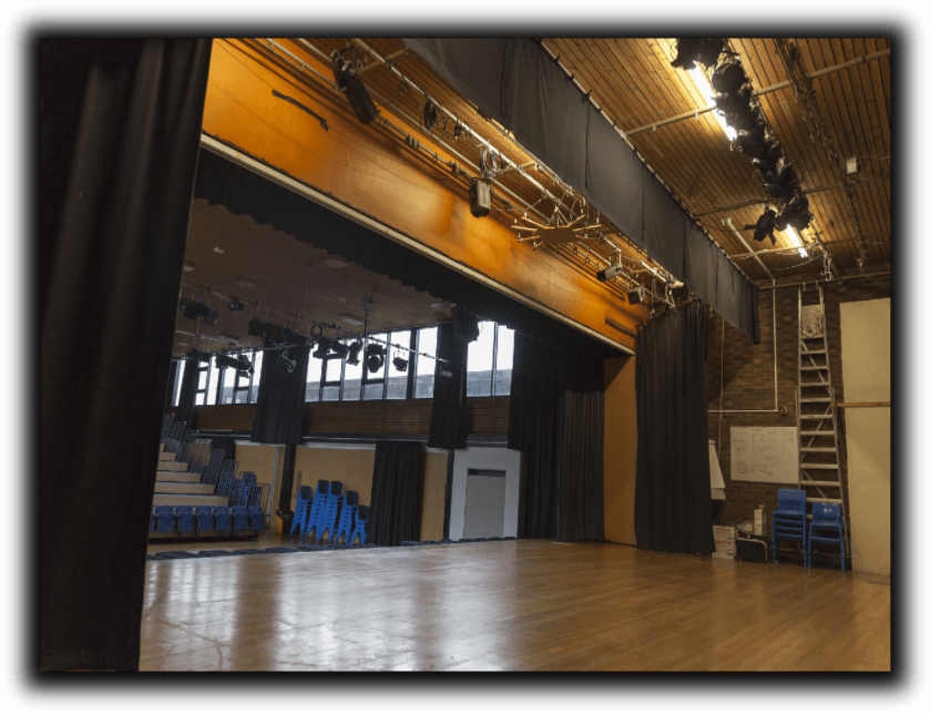 Empty stage with black curtains, wooden floor and high ceiling with lighting and a ladder.