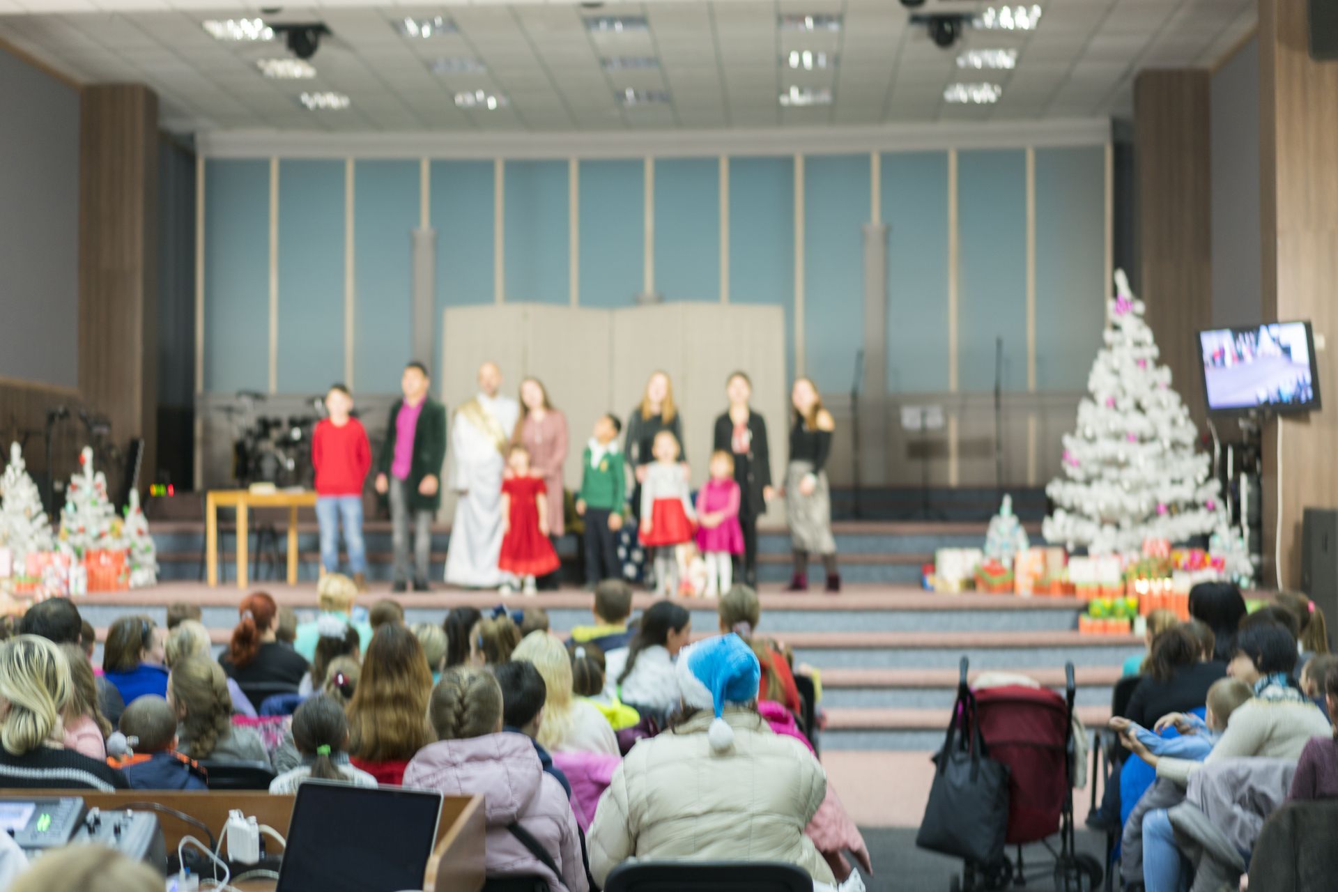 People on stage with Christmas decorations, performing for a seated audience in a hall.