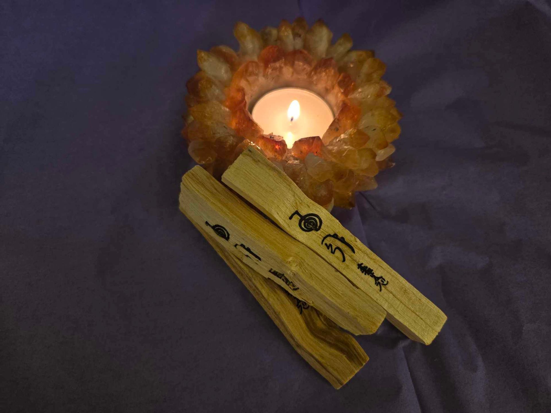 A candle in a crystal holder next to some wooden sticks