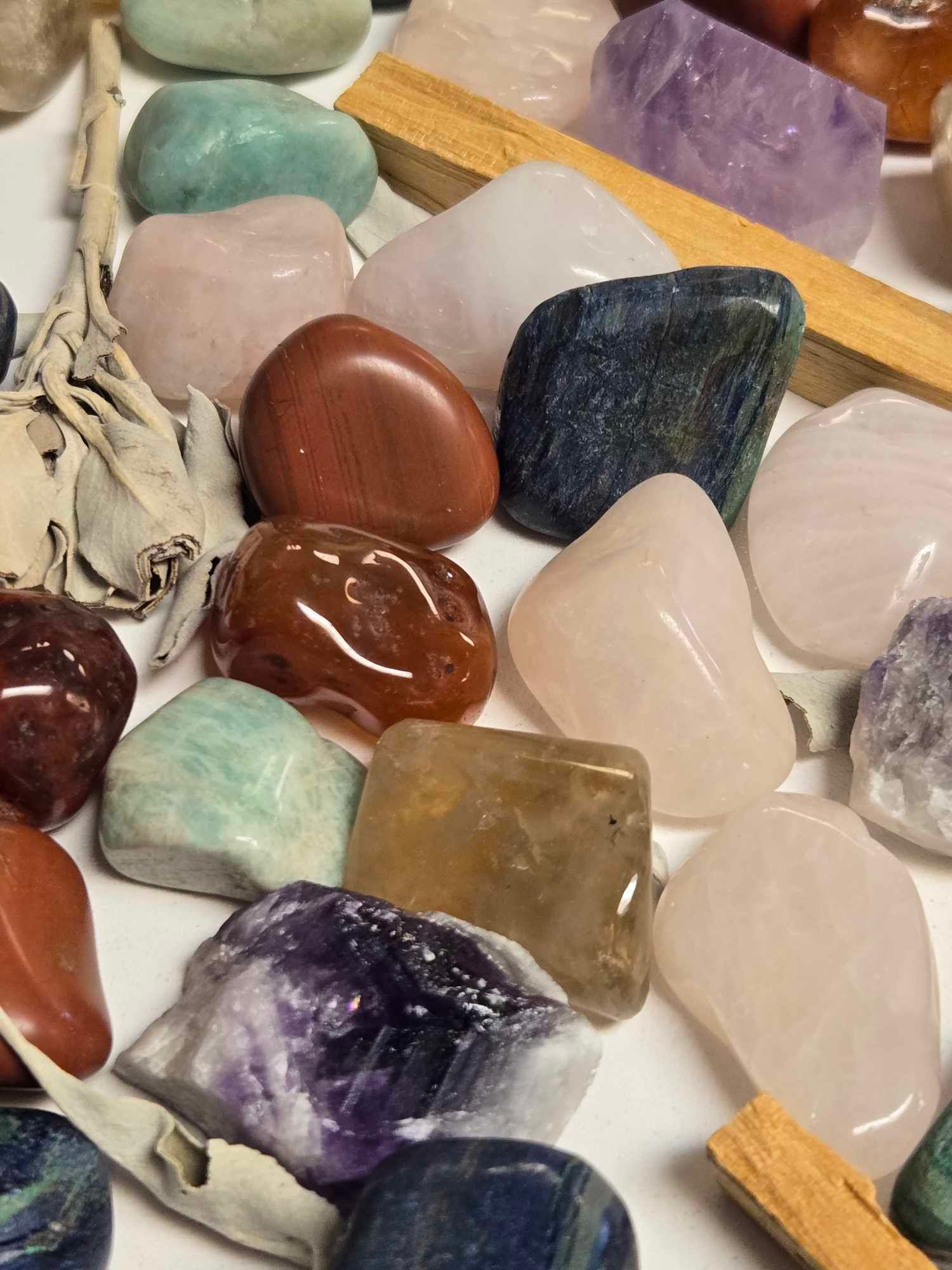 Assorted polished gemstones in various colors with incense sticks and sage on a white surface.