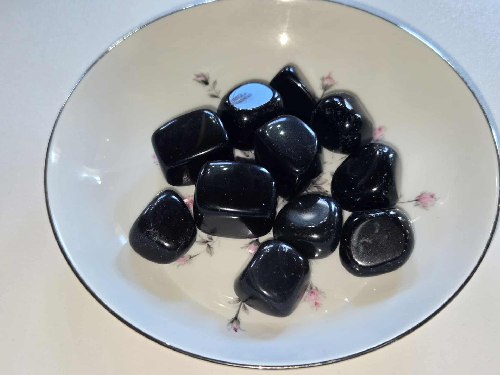 Black polished stones in a floral-decorated white bowl.