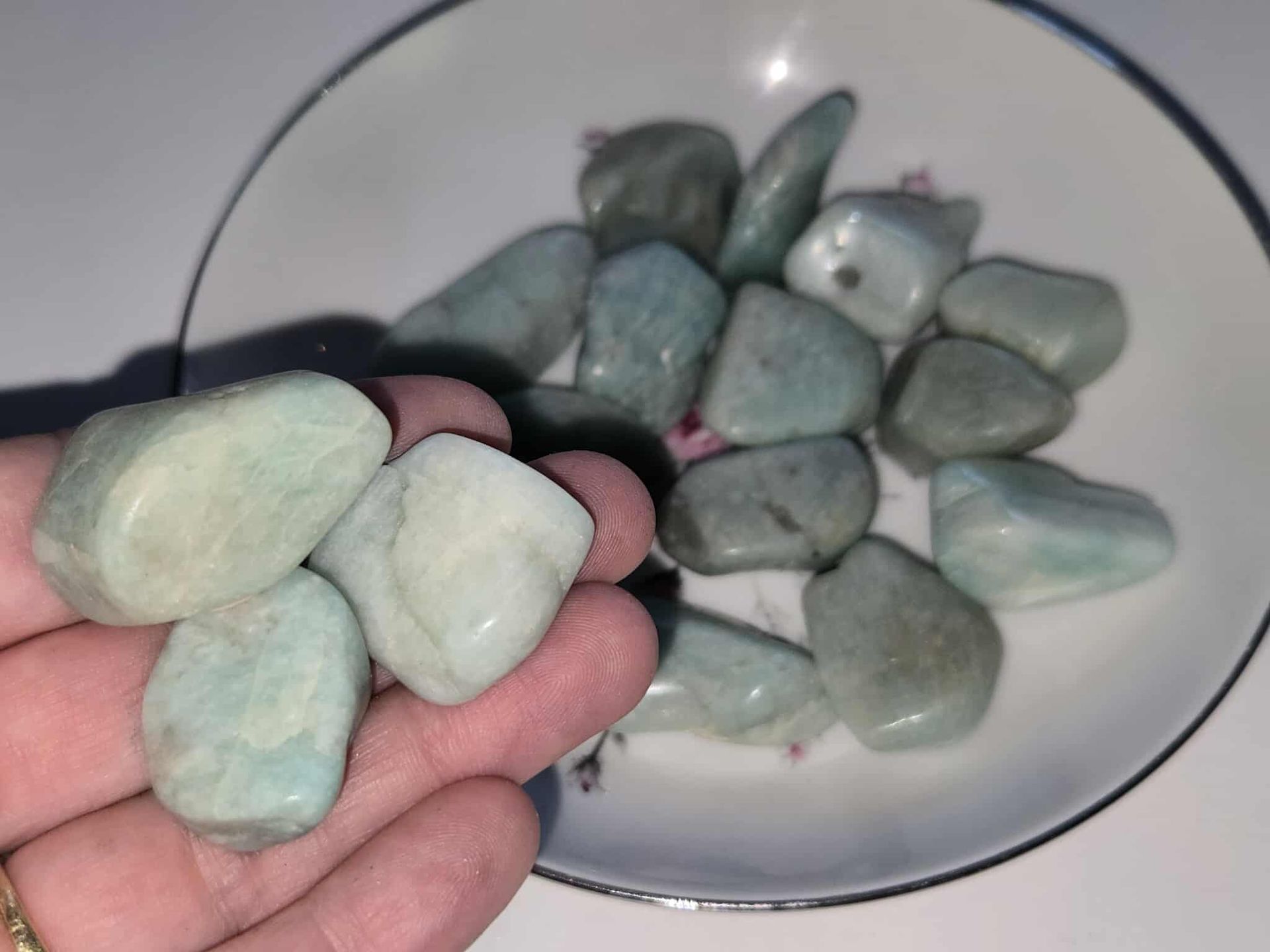 Rounded, teal-green tumbled stones in a white bowl with a dark blue rim.