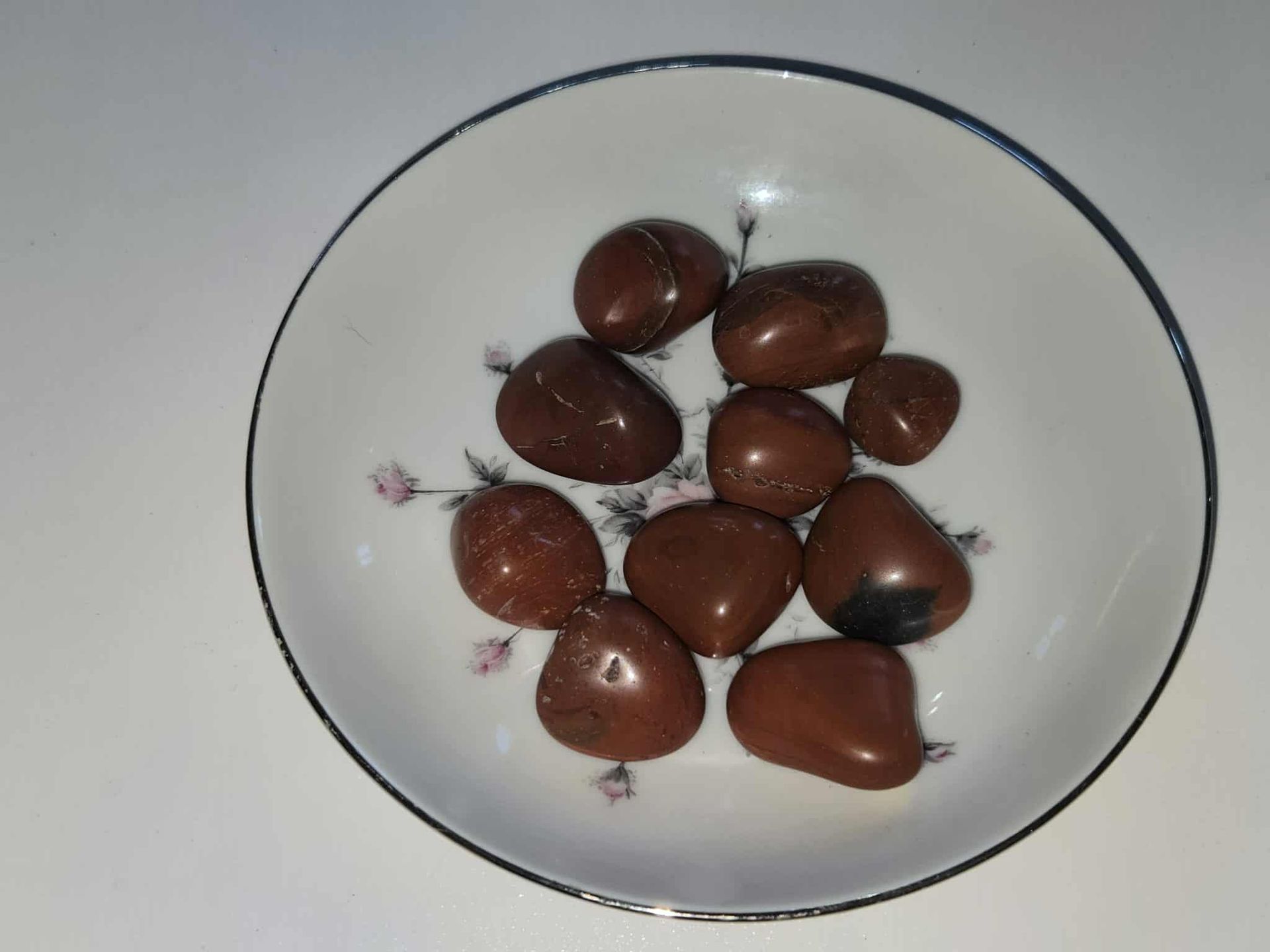 Brown polished stones in a floral decorated white bowl with a blue rim on a white surface.