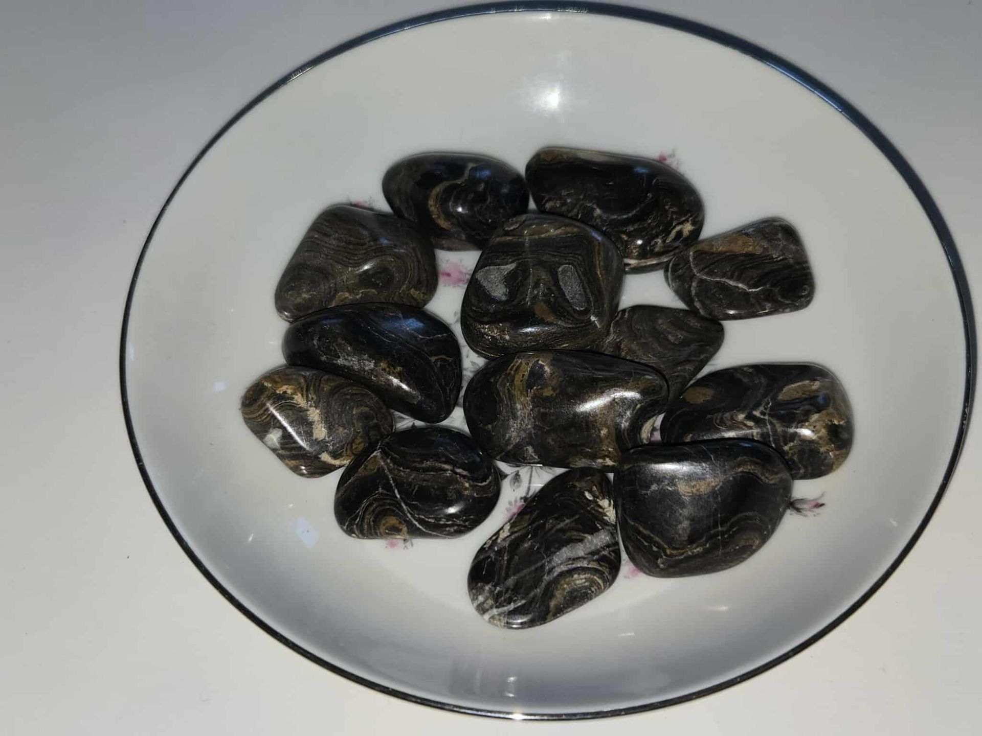 Black polished stones in a white bowl, sitting on a white surface.
