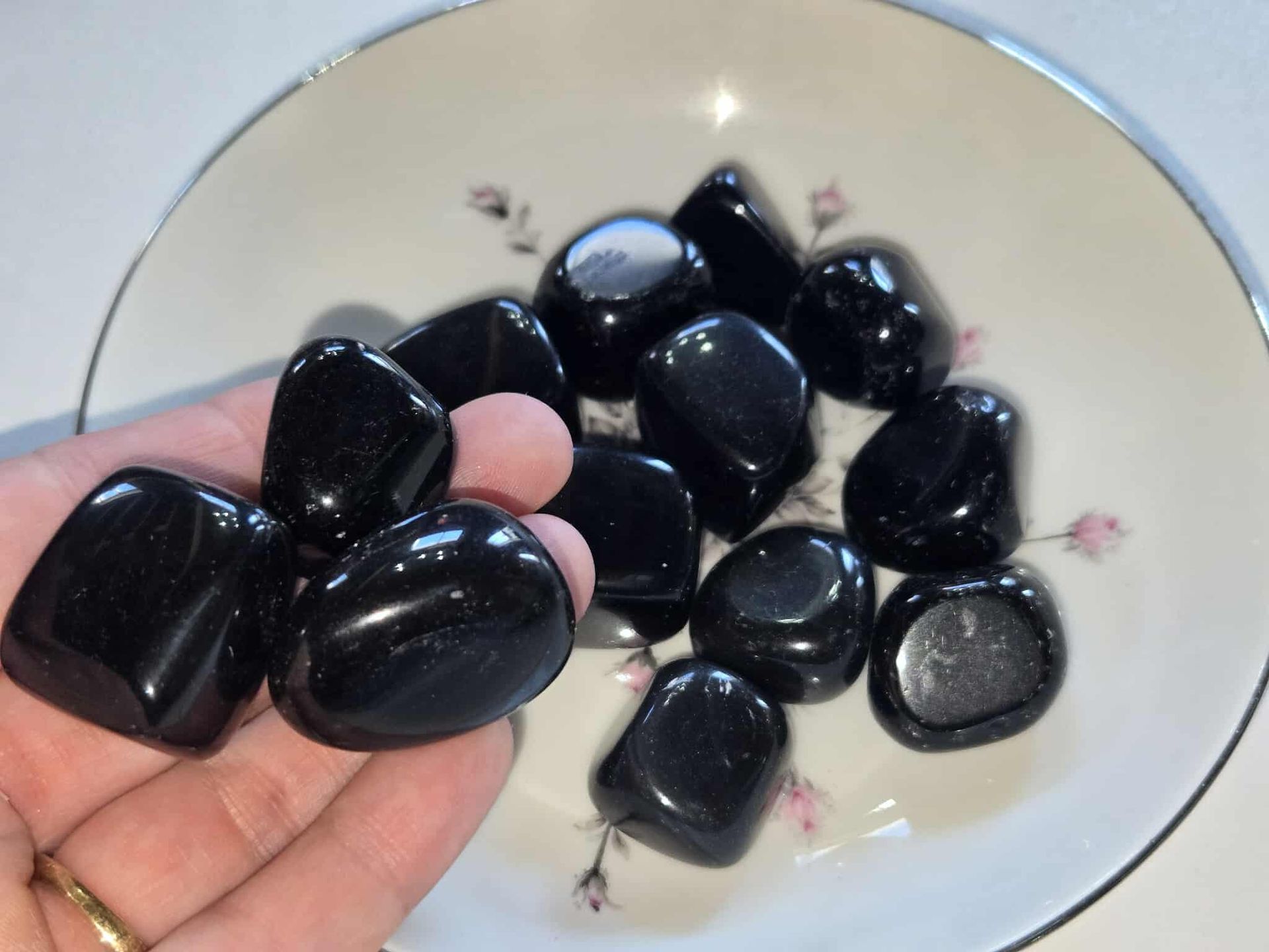 Black polished stones in a floral-decorated white bowl.