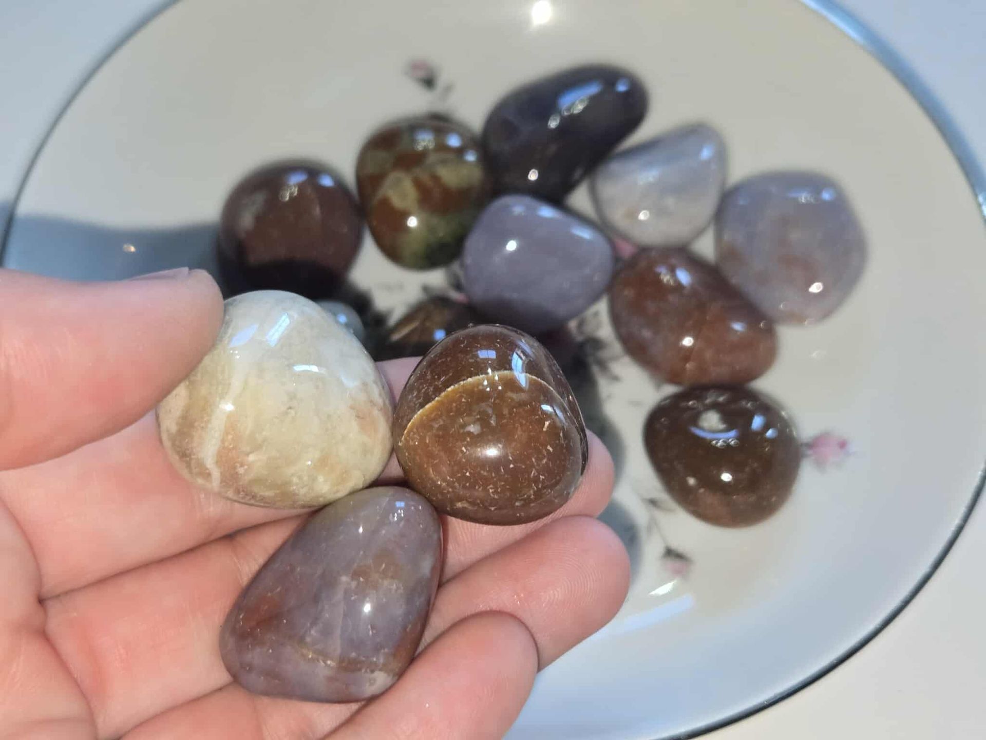 A white bowl with a floral design holds ten polished colorful stones.